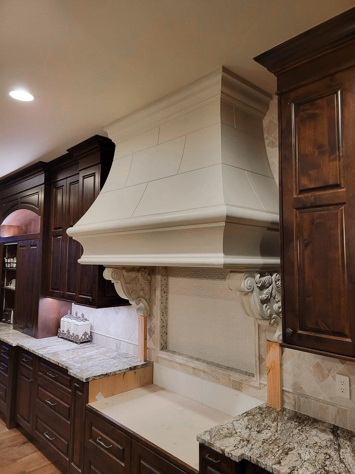 Cream cast-stone fireplace with ornate corbels and stepped mantel shelf in transitional kitchen-dining space.