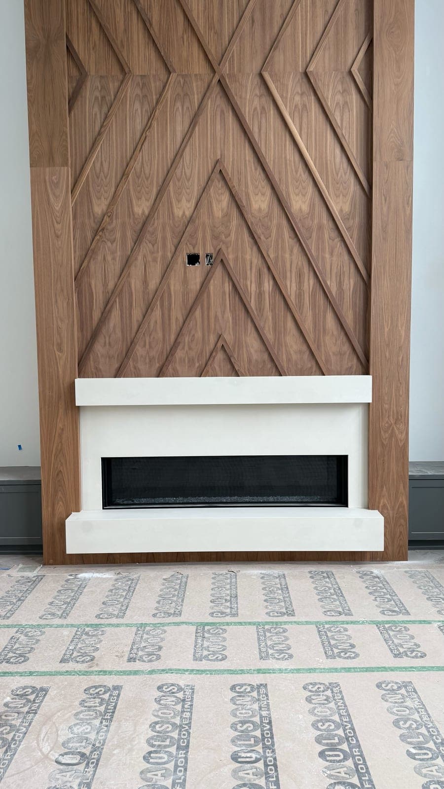 Modern linear fireplace with clean white cast-stone surround and geometric wood accent wall.