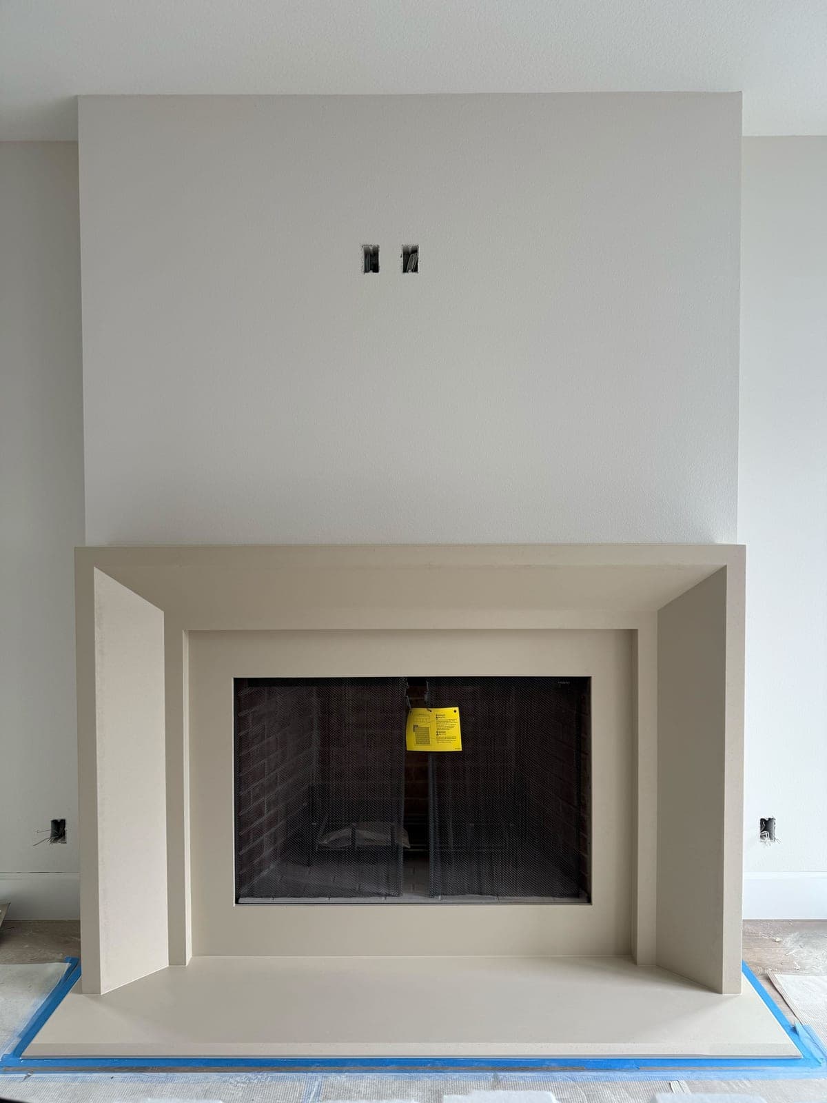 Minimalist modern fireplace surround with clean rectilinear lines and neutral cast-stone finish in construction phase.