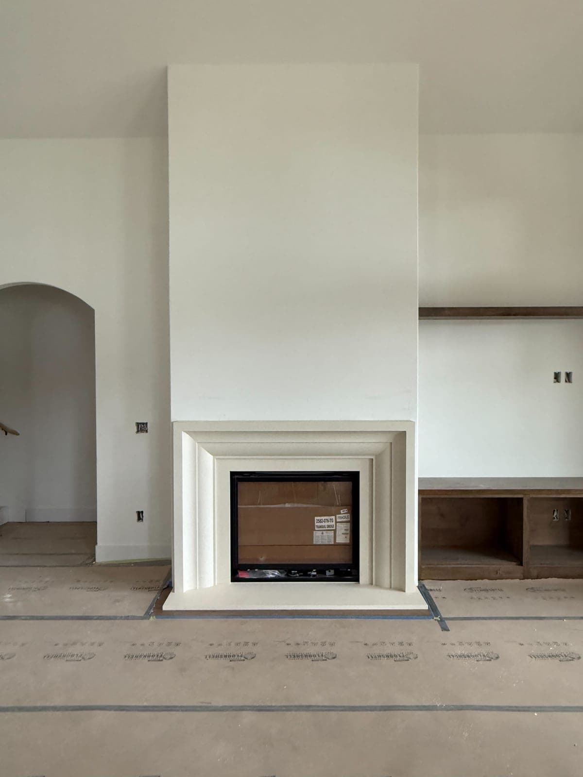 Clean modern cast-stone surround with minimal molding and recessed firebox in construction phase.