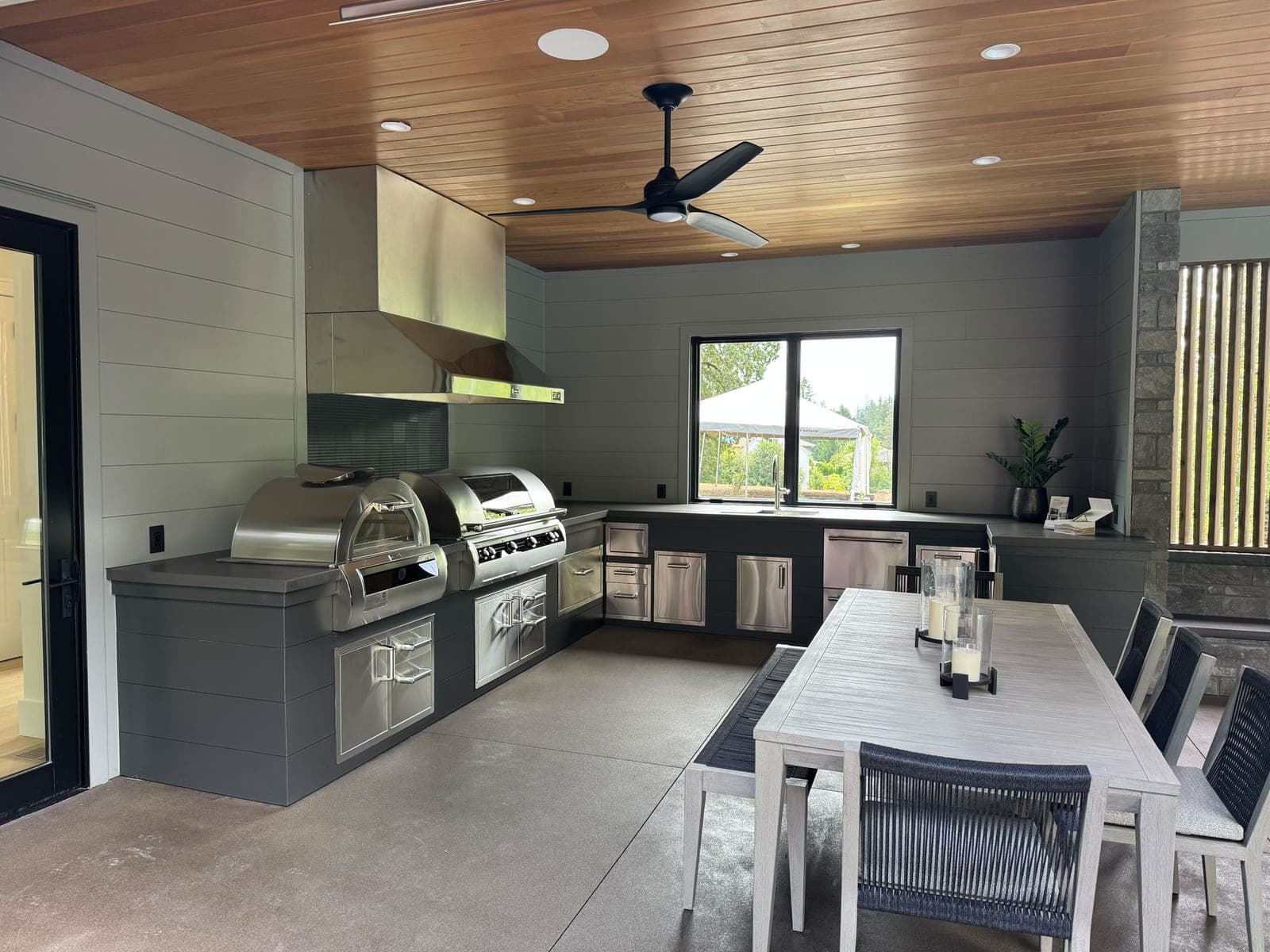 Modern outdoor kitchen and dining pavilion with stainless appliances, no fireplace surround visible.