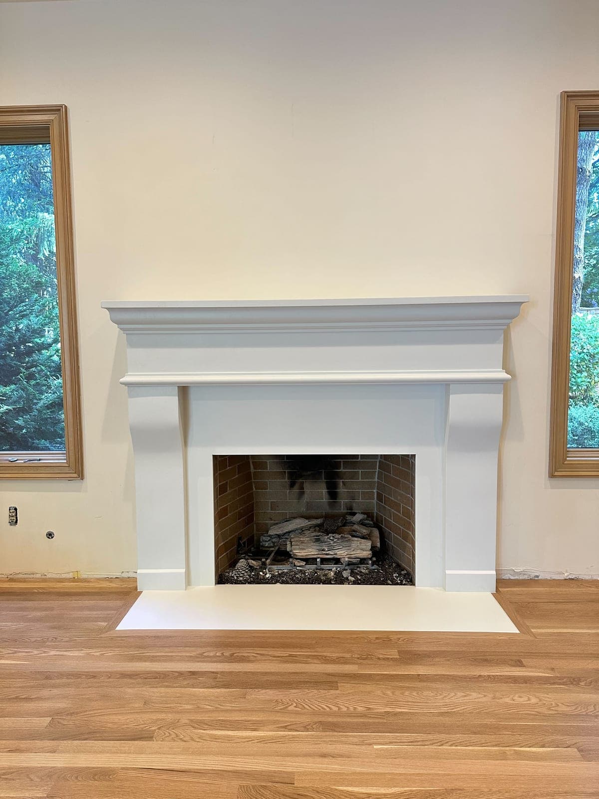 Clean-lined white cast-stone fireplace surround with stepped molding in bright living room with wood flooring.