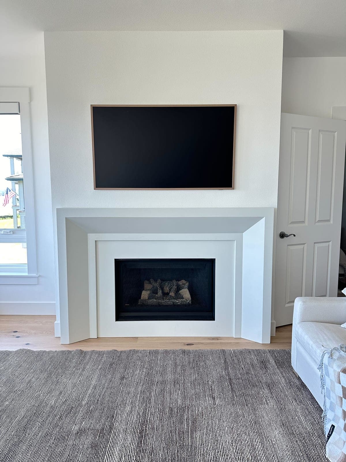 Minimalist white cast-stone fireplace surround with clean rectilinear profile and gas insert in bright living room.