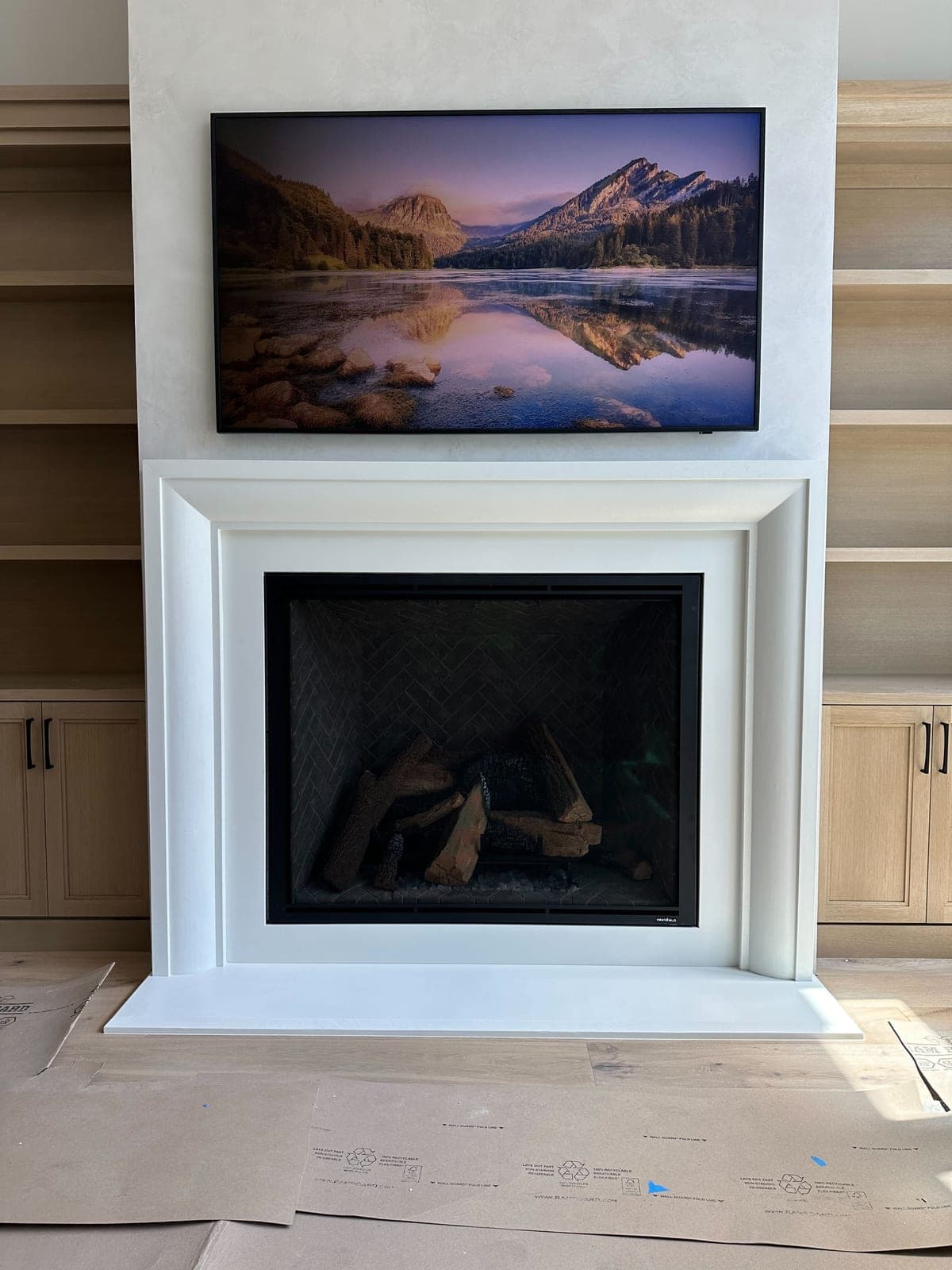 Clean white cast-stone fireplace surround with minimalist framing in bright modern living space under construction.