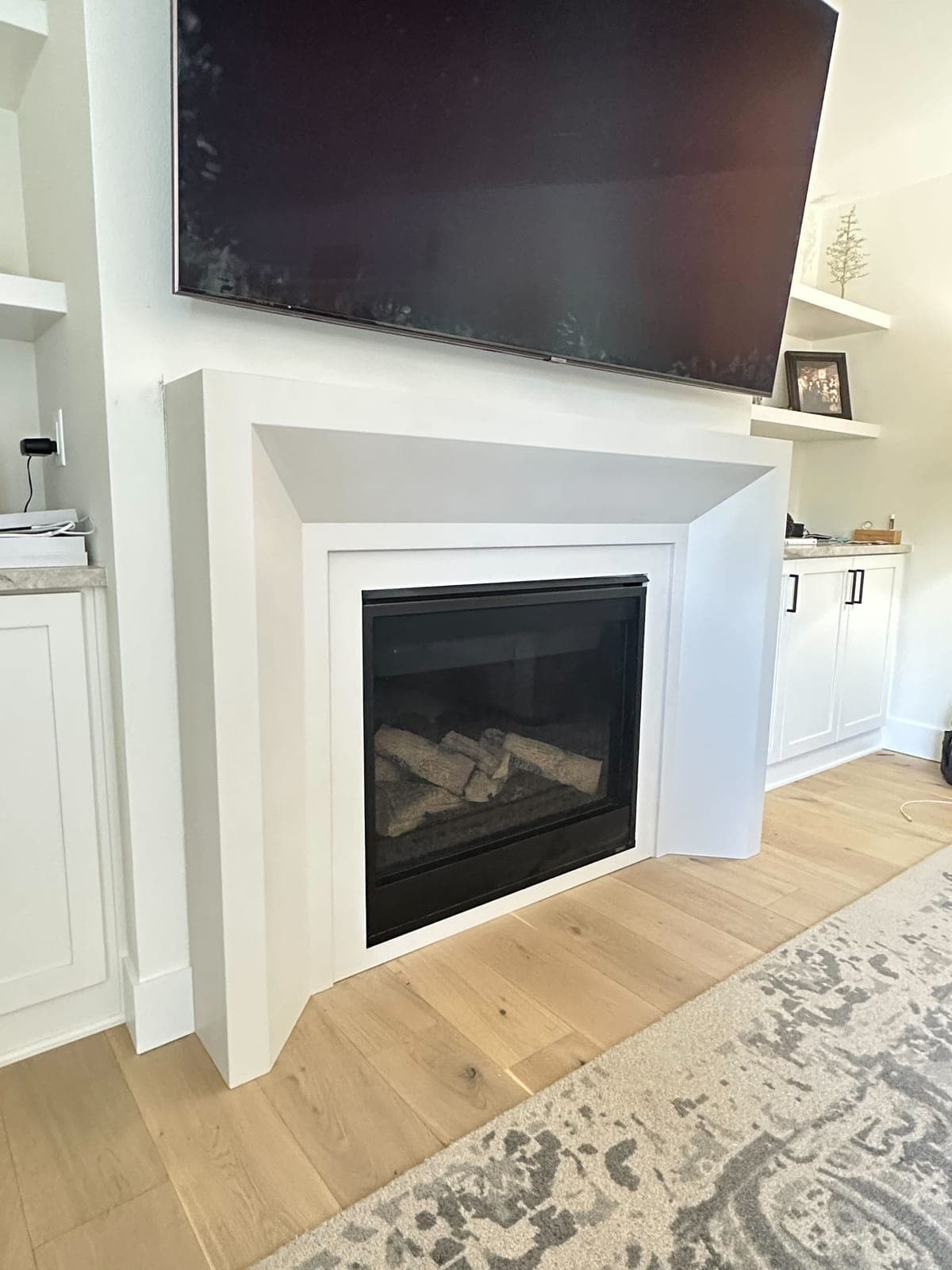 Clean-lined white cast-stone surround with modern angled crown and gas fireplace in contemporary living room.