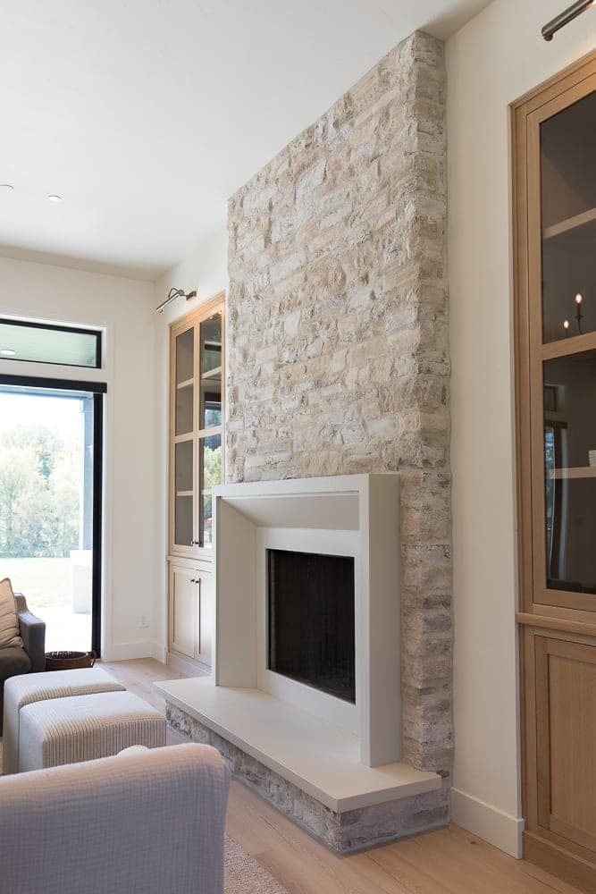 Clean-lined fireplace surround with stacked stone accent wall and minimalist white mantel in bright, modern living space.
