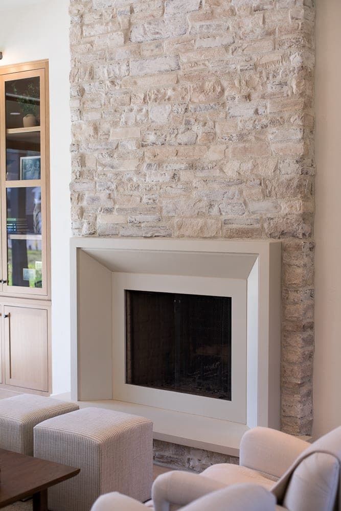 Clean-lined fireplace surround with minimalist profile in cream finish, flanked by natural stone accent wall.