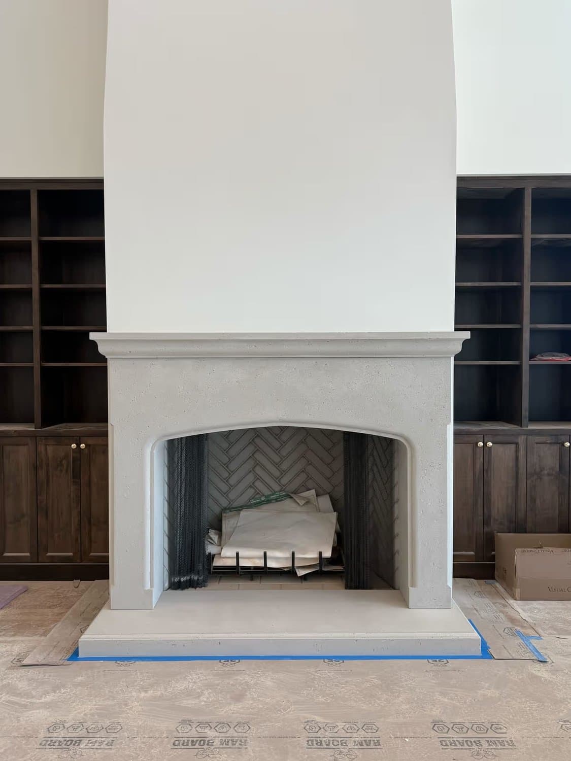 Cast stone fireplace surround newly installed on an active job site, floor protection still in place.